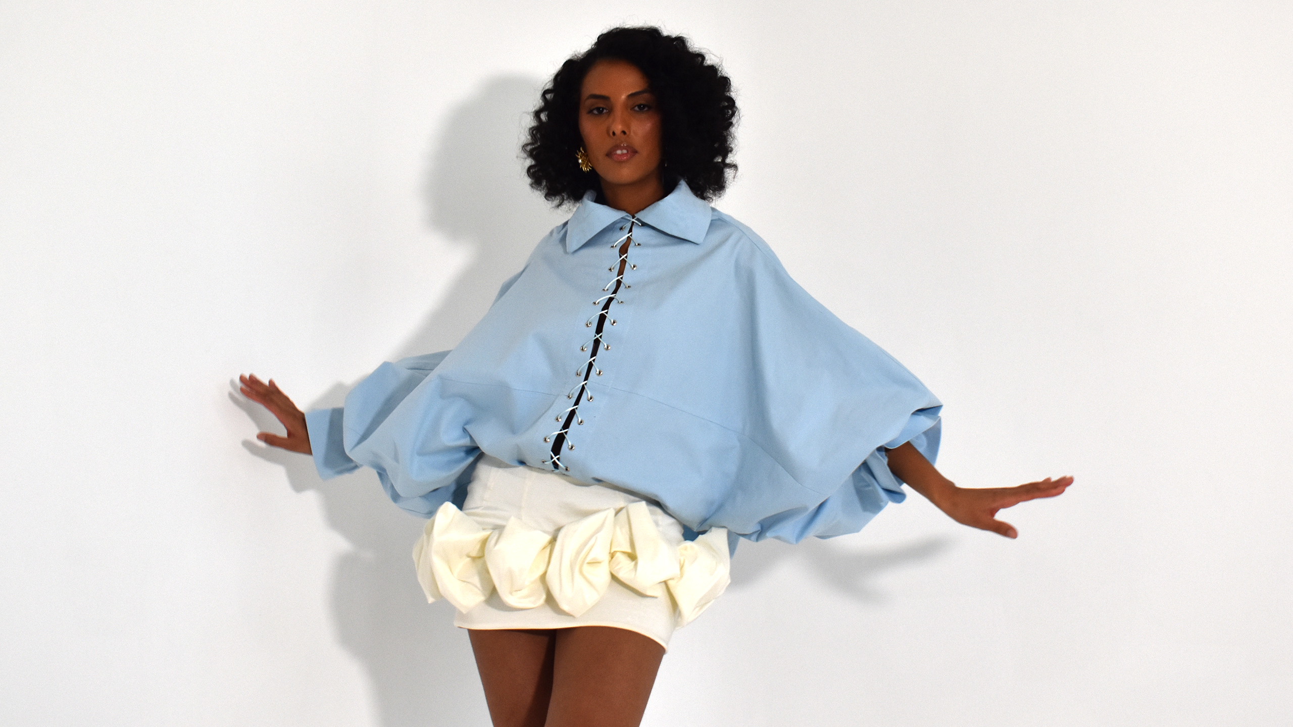 Editorial de moda Madre Atelier — modelo vestindo camisa azul pastel com detalhe de amarração e saia esculpida em tom off-white